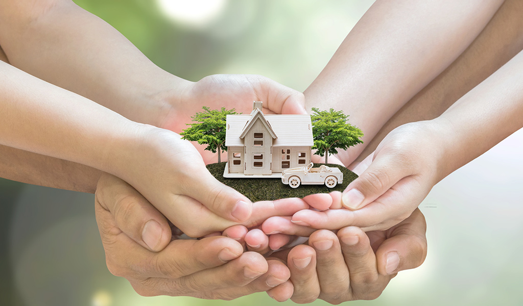 Hands of family members holding a miniature property with a house and car